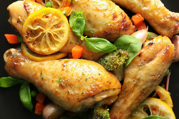 Delicious roasted chicken drumsticks with lemon on plate, closeup