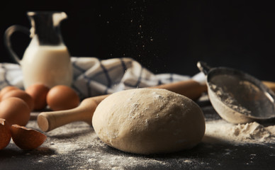Raw dough and ingredients on dark table