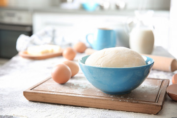 Bowl with raw dough and cutting board on kitchen table