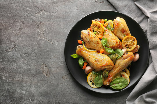 Plate with delicious roasted chicken drumsticks and lemon on grey table