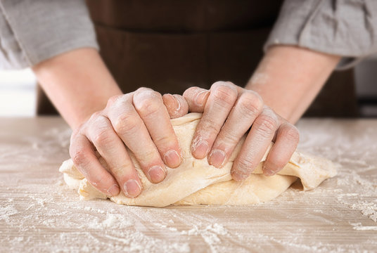 Woman kneading dough on table in kitchen