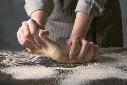 Young woman kneading dough on dark table