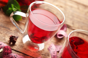 Cups of hibiscus tea and measuring tape on wooden table. Weight loss concept