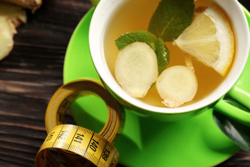 Cup of tea with ginger, mint, lemon and measuring tape on table, closeup. Weight loss concept