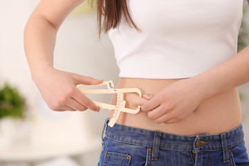 Young woman with measuring caliper on light background. Weight loss concept