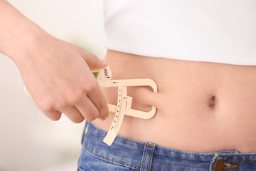 Young woman with measuring caliper on light background, closeup. Weight loss concept