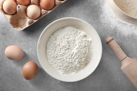 Bowl with white flour, eggs and rolling pin on kitchen table