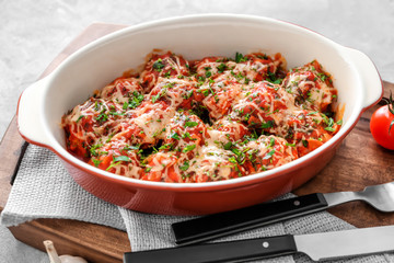 Ceramic casserole dish with turkey meatballs, tomato sauce and melted cheese on wooden board