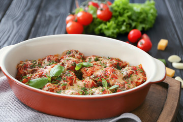 Ceramic casserole dish with turkey meatballs, tomato sauce and melted cheese on table