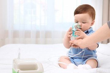 Health care concept. Woman with little baby and nebulizer indoors