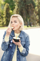 Beautiful young girl eating tasty yogurt ice cream outdoors