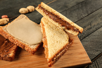 Tasty sandwiches with peanut butter on wooden board