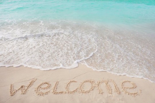 Word WELCOME on beach sand. Summer vacation concept