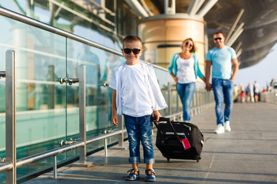 Cute little kid boy with suitcase on international airport. Mother and daughter on background, happy family waiting for flight and going on vacations.