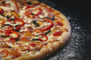 Delicious pizza fresh hot closeup on black table with scattered flour