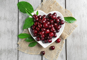 Heart-shaped plate with tasty cherries on wooden background