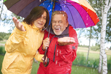 Cheerful couple standing in the autumn rain with umbrella
