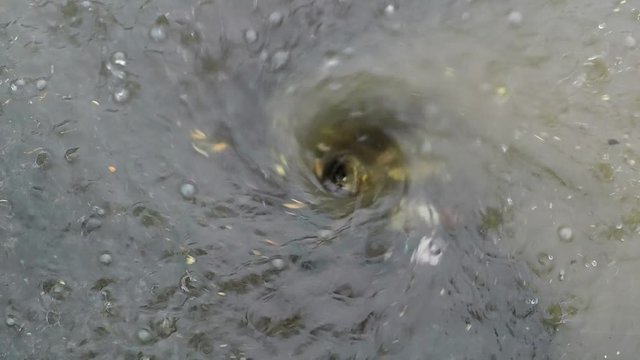 Strong rain causes a flooded road, and a whirlpool over a gutter. 