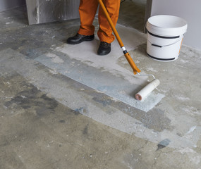 Worker puts primer with roller on concrete floor in room of unfi