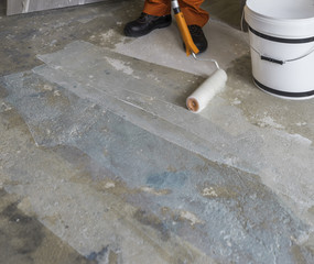 Worker puts primer with roller on concrete floor. Room of house