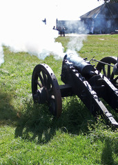 Civil War Era Replica Smooth Bore Field Cannon/Gun Fired and Smoking Against a Grass Background and Unrecognizable Spectators
