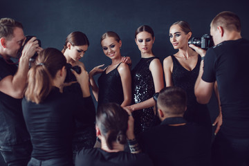 Photographers paparazzi take photos of women in cocktail dresses on dark background.