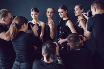 Photographers paparazzi take photos of women in cocktail dresses on dark background.
