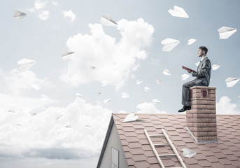 Man on brick roof reading book and paper planes flying in air