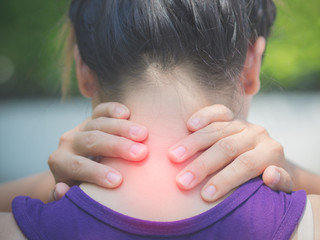Athletic young woman touching her neck by painful injury, over a nature background. Sport injuries concept.