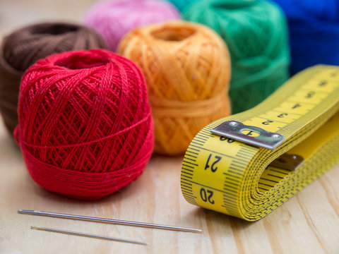 colored woolen thread and needles and meter close up on a wood background