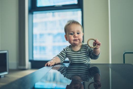 Little baby with teething ring standing at table
