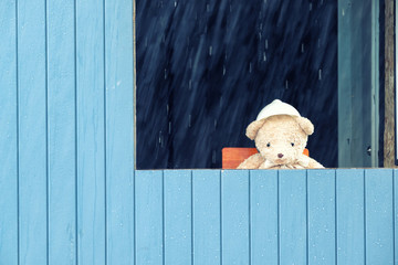 Lonely teddy bear sitting by the window on a rainy day