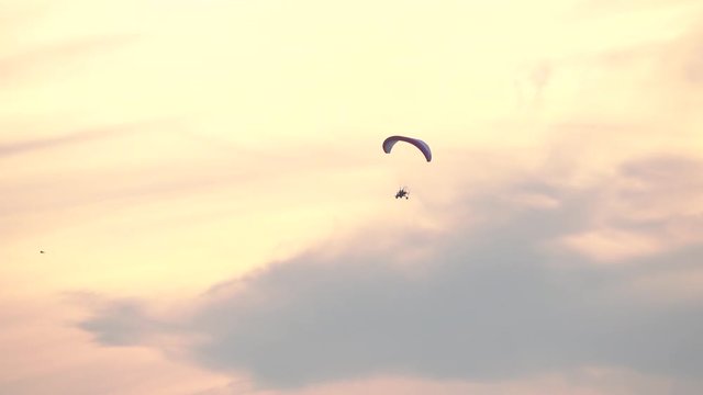 Unknown powered paraglider flying high in sunset sky