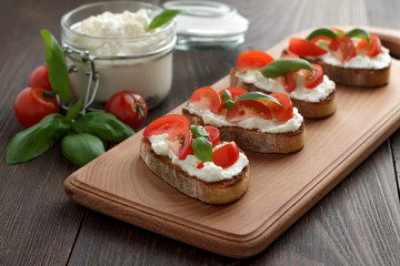 Homemade bruschetta with cheese feta, tomatoes and basil on cutting board on wooden table.