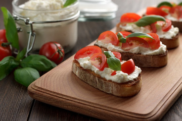 Italian appetizer bruschetta with ciabatta, feta, tomatoes and basil on cutting board.