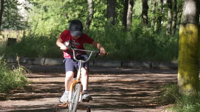 A six year old little boy, making his first steps to ride a four wheeled bicycle in the summer green forest park. Childhood and growth, the first difficult steps of people and learning concept.