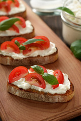 Mediterranean appetizer bruschetta with cheese, tomato and basil on cutting board.