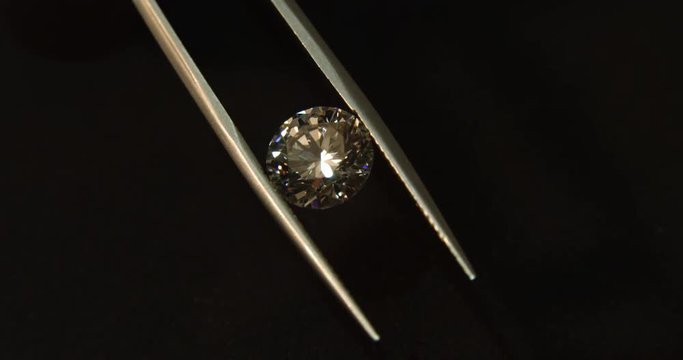 brilliant cut diamond held with the nipper shines over black background close up