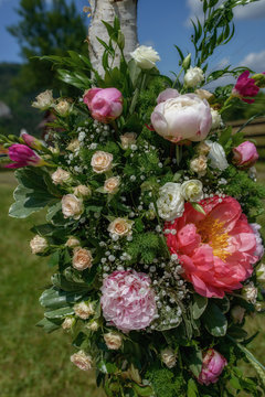 Close-up of lush floral arrangement featuring peonies, roses and freesias, decorating trees at the outdoor location for the wedding ceremony, beautiful bouquet prepared as decor