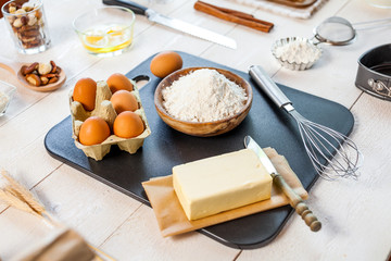 Baking ingredients in rural kitchen - dough recipe ingredients (eggs, flour, milk, butter, sugar) and rolling pin on wooden white table.