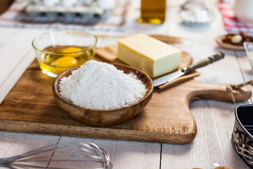 Baking ingredients in rural kitchen - dough recipe ingredients (eggs, flour, milk, butter, sugar) and rolling pin on wooden white table. Close up