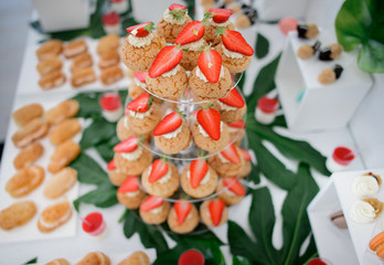Strawberry eclairs served on transparent dish stand on a table with other sweets