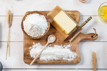 Baking ingredients in rural kitchen - dough recipe ingredients (eggs, flour, milk, butter, sugar) and rolling pin on wooden white table. Top View