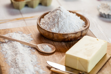 Baking ingredients in rural kitchen - dough recipe ingredients (eggs, flour, milk, butter, sugar) and rolling pin on wooden white table. Close up