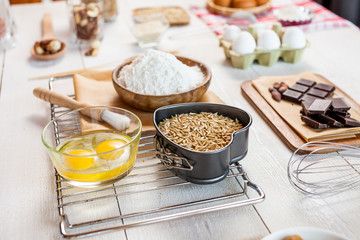 Baking ingredients in rural kitchen - dough recipe ingredients (eggs, flour, milk, butter, sugar) and rolling pin on wooden white table.
