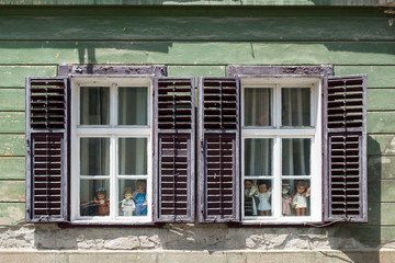 Detail of facade with old windows in rustic ancient house in Sibiu city, various old dolls in the window, Romania
