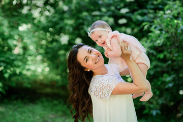 Pretty brunette woman in white dress poses with her little daughter in the garden