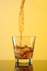Whiskey splash out of glass on yellow background