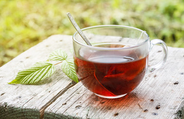 Big transparent cup of tea on a wooden table with green leaves on it