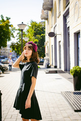 Fototapeta premium Beautiful woman in a dark stylish dress strolls along the street, near boutiques. Portrait of a fashionable girl